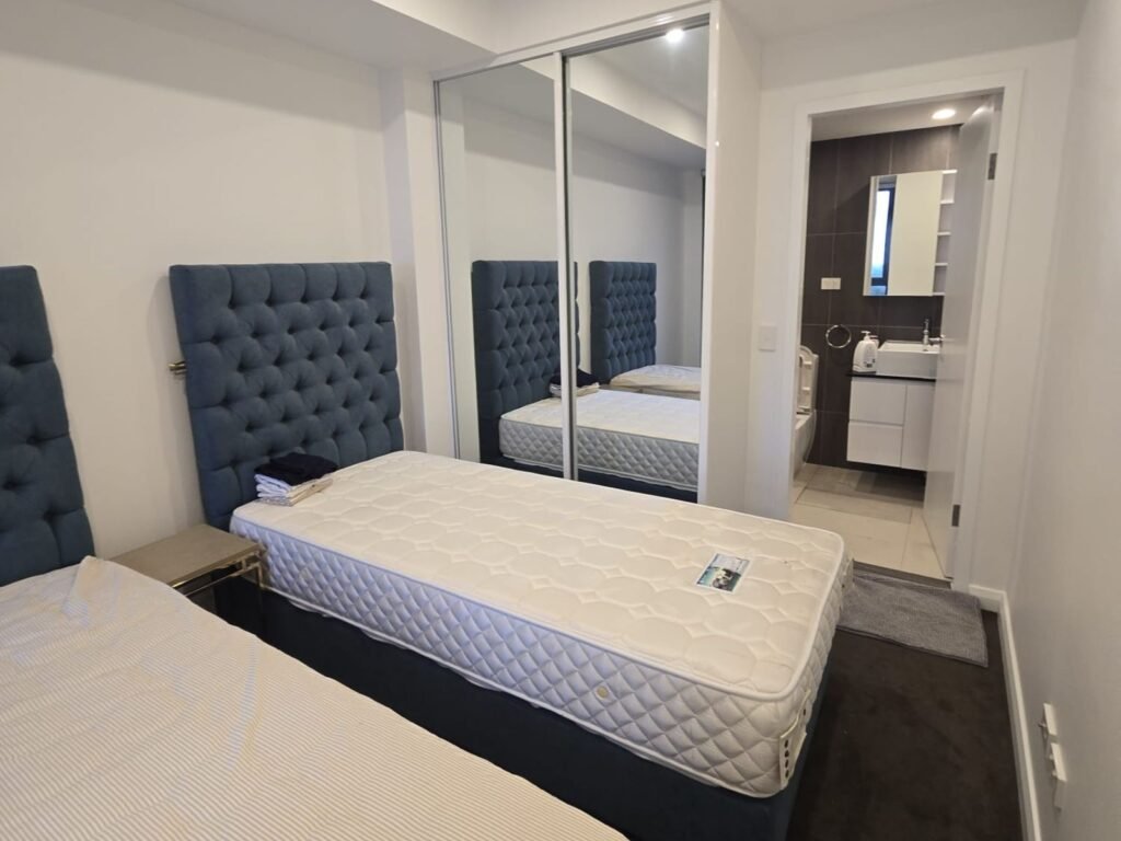 Furnished twin-share room with blue headboards and mirrored wardrobe at Stay Spot shared accommodation in Parramatta
